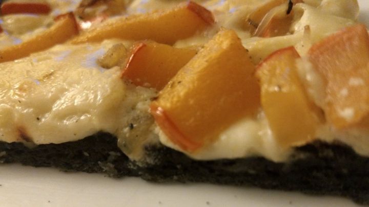 Eine Halloween-Pizza ist auf einem wei&szlig;en Teller zu sehen, belegt mit K&uuml;rbisst&uuml;cken und Zwiebeln, die appetitlich angeordnet sind.