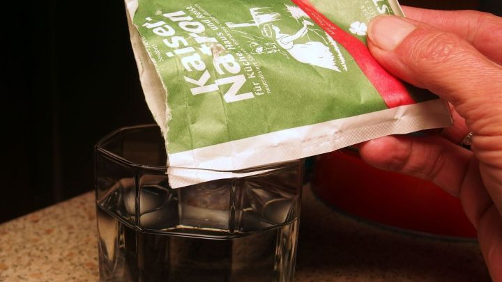 Eine Hand h&auml;lt ein Paket mit einem Erk&auml;ltungsgetr&auml;nk &uuml;ber ein Glas mit Wasser, um es nach Alkoholgenuss zuzubereiten.