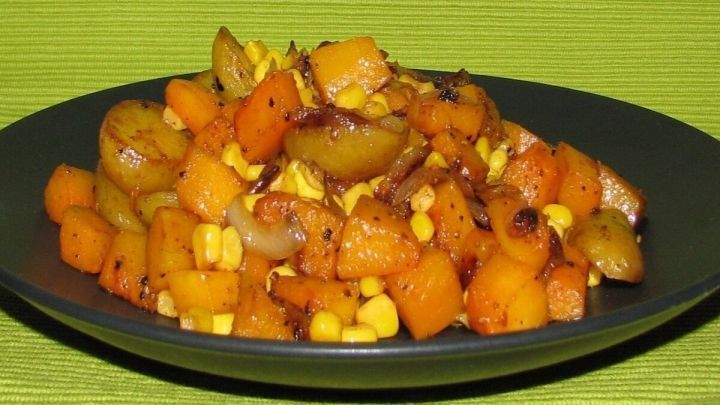 Bunte K&uuml;rbisst&uuml;cke und Mais sind auf einem schwarzen Teller angerichtet und heben sich vor einem gr&uuml;nen Hintergrund ab.