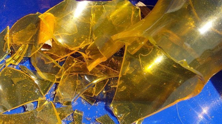 Zersplitterte Glasreste liegen auf einem blauen Untergrund, nachdem eine volle Flasche heruntergefallen ist.