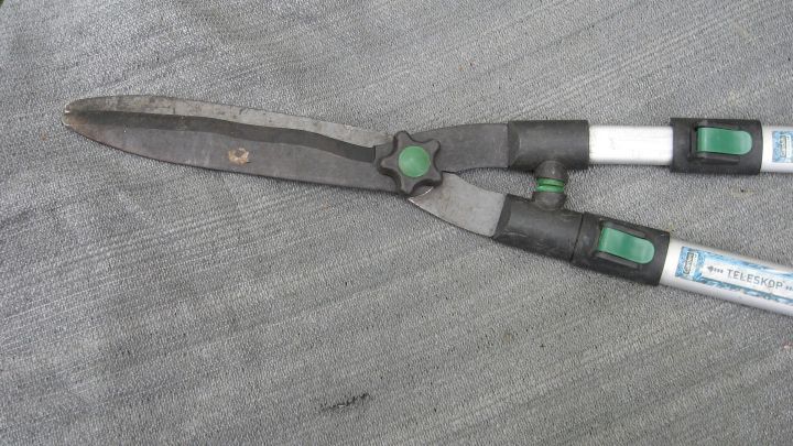 Eine Heckenschere liegt auf einer grauen Unterlage, bereit zur Reparatur, um den Hebelarm wieder funktionsf&auml;hig zu machen.