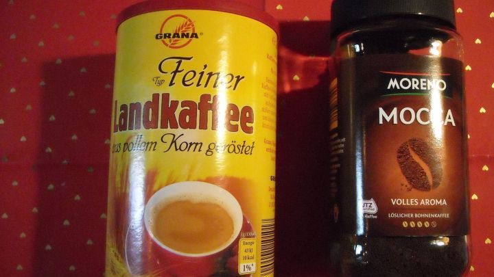 Zwei Kaffeeprodukte stehen auf einem roten Tisch: ein gelbes D&ouml;schen mit "Feiner Handkaffee" und ein schwarzes Glas mit "Moredo Moca".