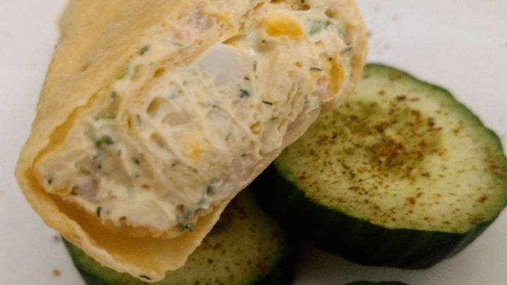 Ein knuspriger Wrap mit cremiger F&uuml;llung liegt neben gew&uuml;rzten Gurkenscheiben als erfrischende Beilage.