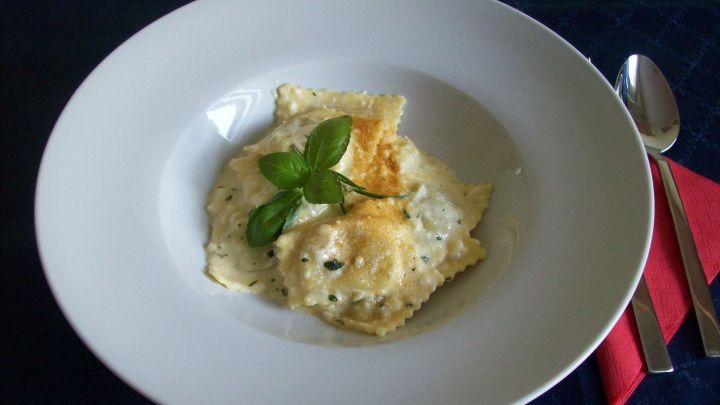Pasta mit Camembert-Creme liegt in einem wei&szlig;en Teller, dekoriert mit einem Basilikumblatt auf einem blauen Tisch.