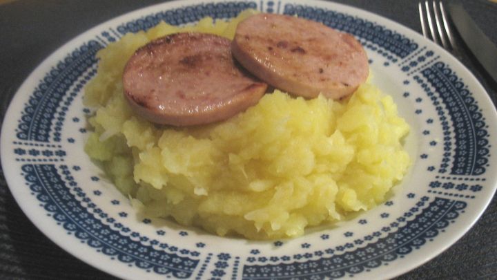 Ein Teller mit cremigem Strohlehme ist mit gebratenen Scheiben Strupsch belegt, serviert auf einem gemusterten Teller.