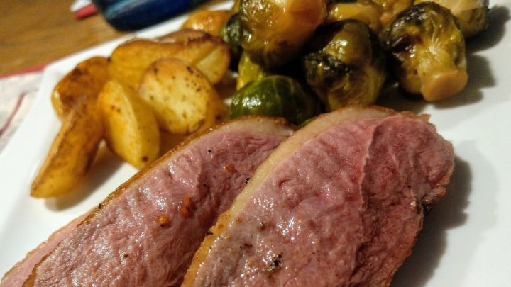 Zarte Entenbrust liegt auf dem Teller, nebeneinander mit karamellisiertem Rosenkohl und knusprigen Kartoffelecken.