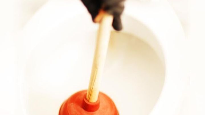 Ein P&ouml;mpel wird von einer Hand in eine verstopfte Toilette gehalten, um die Verstopfung zu l&ouml;sen.