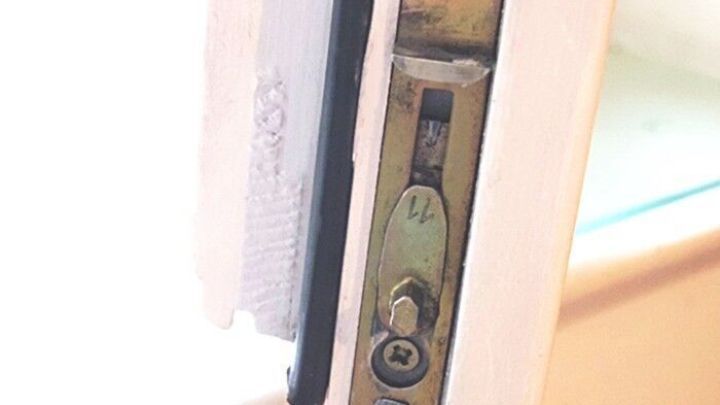 Ein Fensterscharnier befindet sich an einem Fensterrahmen und zeigt eine Reinigung oder Pflege. Der Umgebungsbereich ist hell und zeigt einen Teil des Fensters.