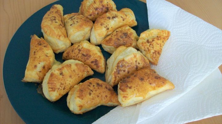 K&auml;sehappen liegen auf einem gr&uuml;nen Teller, leicht goldbraun und knusprig, umgeben von einem Papiertuch.