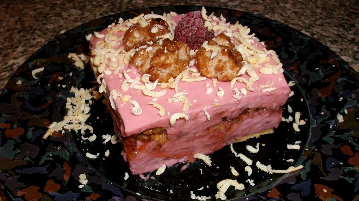 Ein rosa Himbeer-Mascarpone-T&ouml;rtchen liegt auf einem dekorativen Teller, garniert mit Waln&uuml;ssen und Schokoladenraspeln.