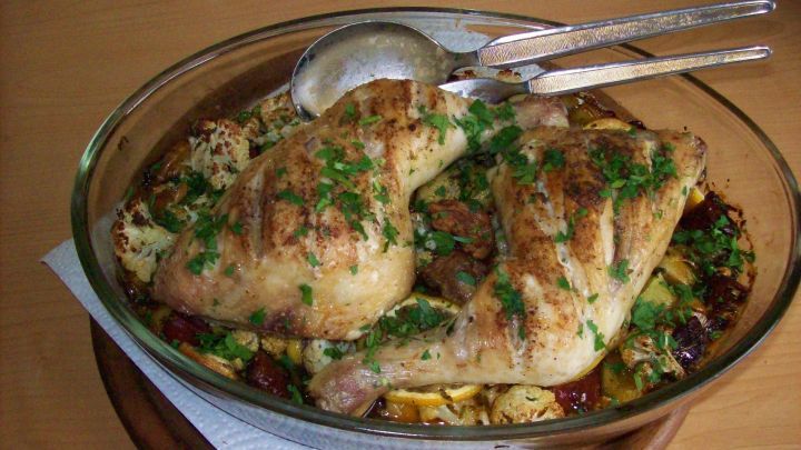 In einer Glassch&uuml;ssel sind gebratene H&auml;hnchenkeulen mit Blumenkohl und frischer Petersilie angerichtet, umgeben von Gem&uuml;se.