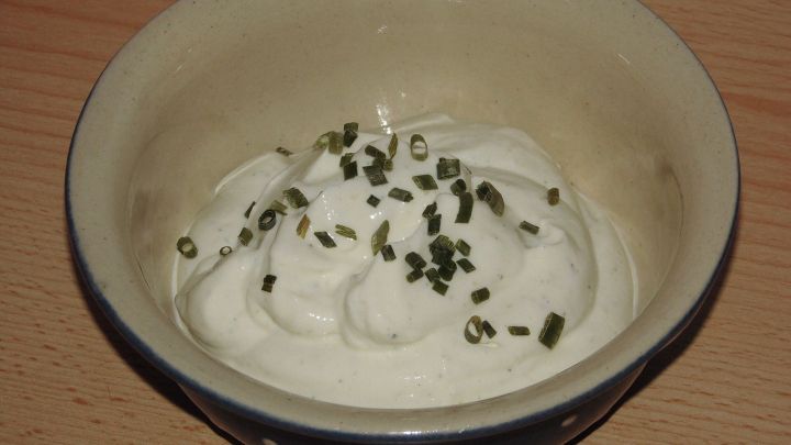 Ein Dip aus Joghurt und Kr&auml;utern wird in einer Schale serviert, umgeben von einer holzartigen Tischoberfl&auml;che.