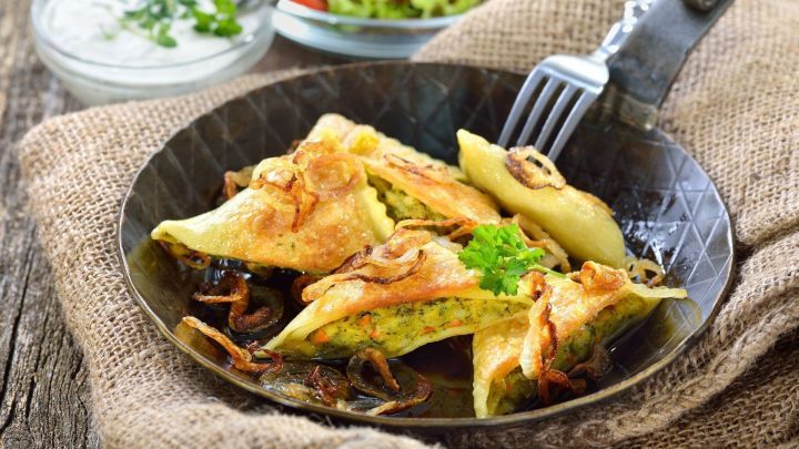 Krosse, frittierte Maultaschen liegen auf einem dunklen Teller, umgeben von Salat und einem Dip in einer Schale.