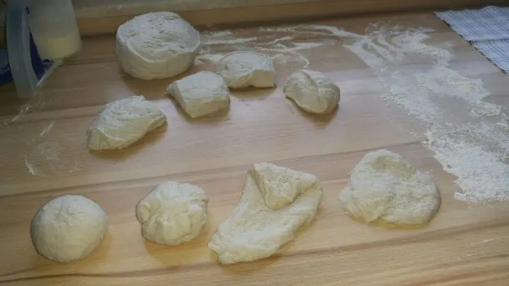 Nachdem der Teig vorbereitet wurde und gehen konnte, wird er geknetet, gerollt und in Teiglinge geschnitten. Die werden flach gedrückt und gezogen, bis sie fast rund sind, und dann zur Kugel gerollt.
