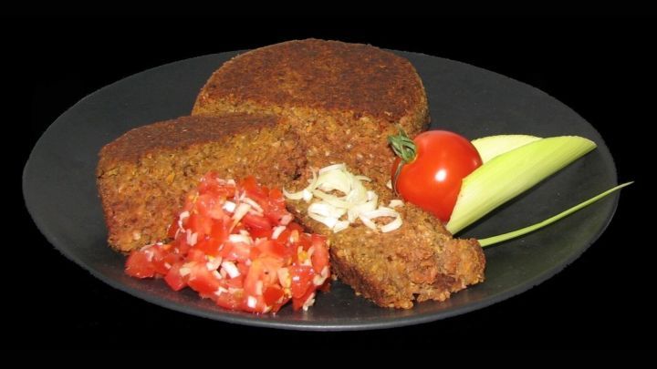 Der vegane Buchweizen-Hackbraten liegt auf einem schwarzen Teller, umgeben von frischem Gem&uuml;se und einer Tomatensalsa.