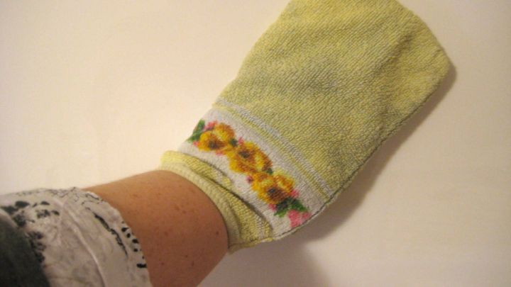 Ein gelber Waschlappen mit Blumenmustern wird von einer Hand gehalten, bereit zum Putzen und Staubwischen.