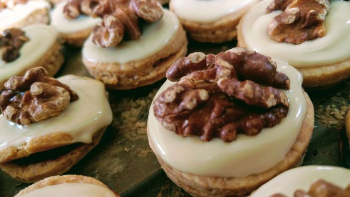 Kleine Keksgeb&auml;cke, die mit einer Schicht aus wei&szlig;er Creme und einer Walnuss belegt sind, auf einer Backform angeordnet.