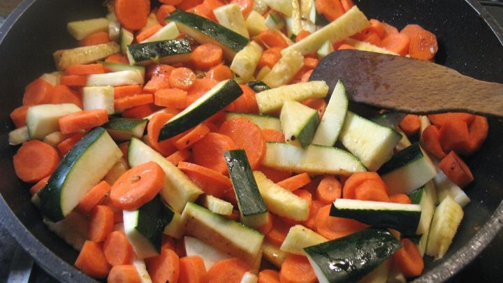 Bunte Zucchini- und Karottenst&uuml;cke werden in einer Pfanne mit einem Holzl&ouml;ffel gemischt, um ein schnelles Pfannengericht zuzubereiten.