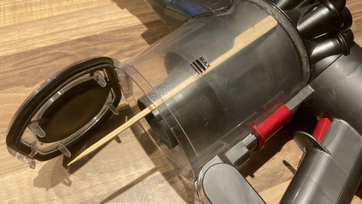 Der Akku-Handstaubsauger mit ge&ouml;ffnetem Beh&auml;lter zeigt, wie man ihn entleert, auf einem Holzfu&szlig;boden.