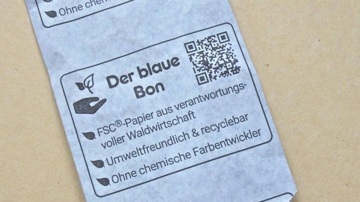 Der blaue Kassenzettel liegt auf einem hellen Hintergrund und zeigt umweltfreundliche Informationen sowie einen QR-Code.