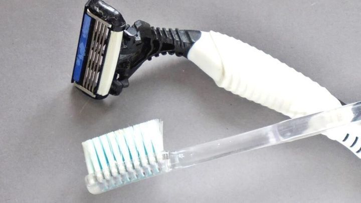 Ein Einweg-Rasierer und eine Zahnb&uuml;rste liegen nebeneinander auf einer grauen Fl&auml;che, bereit zur mehrfachen Verwendung.