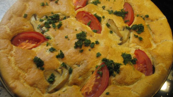 Pikante Eier-Dinkel-Pfanne mit Tomaten und Kr&auml;utern ist goldbraun gebacken und auf einem schwarzen Untergrund pr&auml;sentiert.