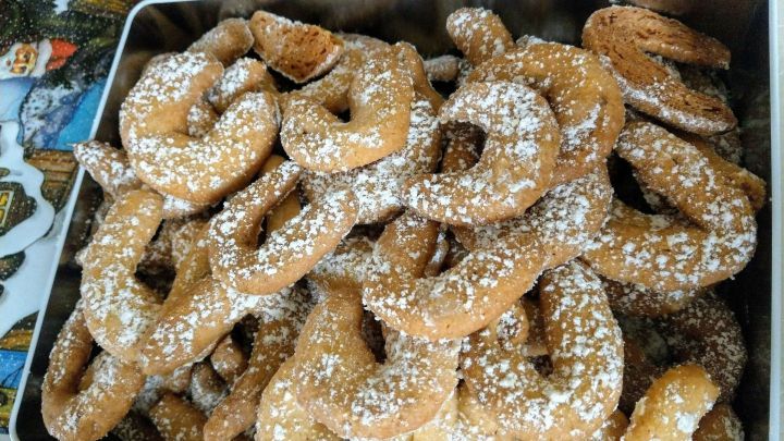 Pl&auml;tzchen aus Vanillekipferl liegen in einer Dose, staubzuckerbest&auml;ubt, bereit zum Genie&szlig;en in einer festlichen Umgebung.