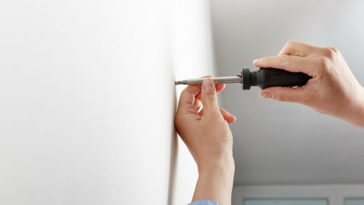 Eine Hand h&auml;lt einen Schraubendreher, w&auml;hrend eine Schraube in einen D&uuml;bel in einer wei&szlig;en Wand eingedreht wird.