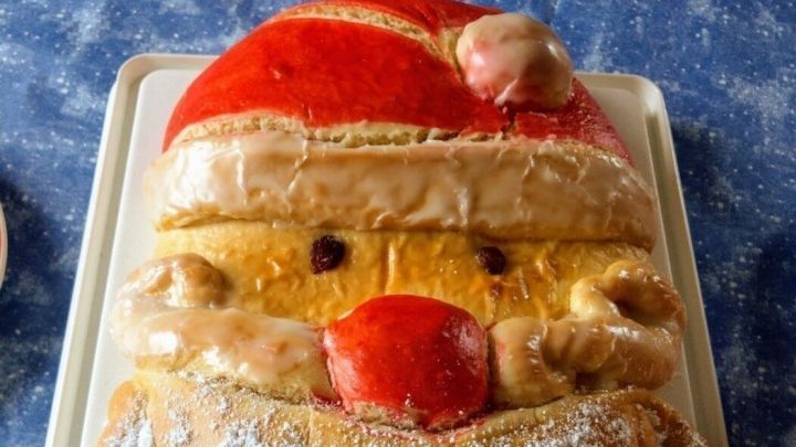 Ein kunstvoll gestalteter Weihnachtsmann aus Hefeteig mit Zuckerguss und Puderzucker auf einem wei&szlig;en Brett.