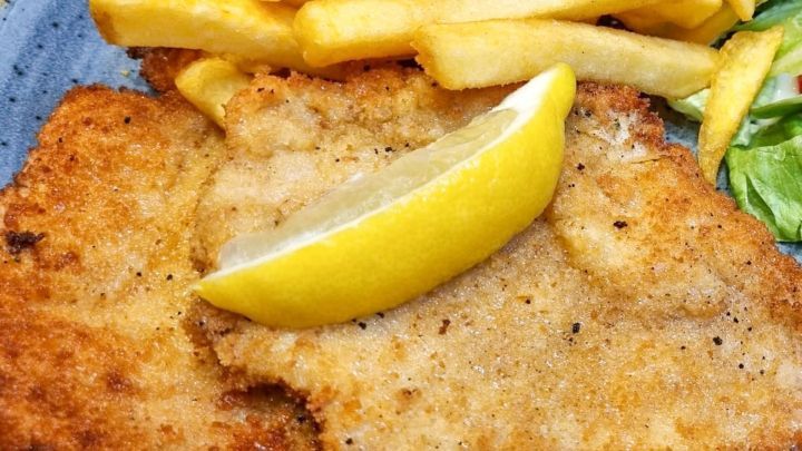 Zwei saftige Schnitzel liegen auf einem blauen Teller, garniert mit einer Zitronenscheibe, daneben gibt es Pommes frites.