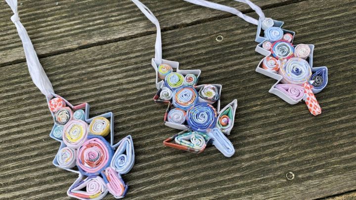 Bunte Tannenbaumschmuck aus Altpapier h&auml;ngt an F&auml;den, auf einer Holzoberfl&auml;che platziert, ideal f&uuml;r DIY Recycling.