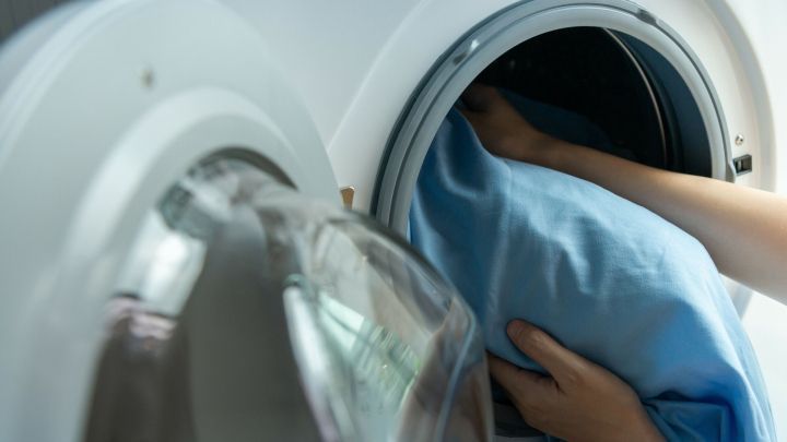Ein hellblaues Bettlaken wird schonend in eine Waschmaschine gelegt, um es sanft zu reinigen.