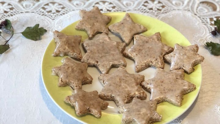 Auf einem gelben Teller liegen liebevoll dekorierte vegane Zimtsterne, umgeben von festlichem Tannengr&uuml;n.