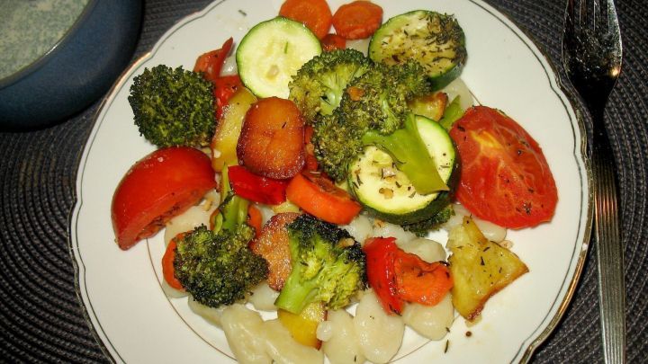 Bunt gebackenes Gem&uuml;se aus Brokkoli, Karotten und Zucchini liegt auf einem Teller, umgeben von Kr&auml;uter-Schmand.