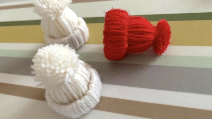 Kleine, handgemachte M&uuml;tzen aus Wolle liegen auf einem gestreiften Tisch, idealer Baumschmuck f&uuml;r die Weihnachtszeit.