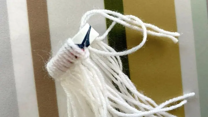 Hier wird ein aus Papierstreifen gefalteter Papierring mit Fäden umwickelt