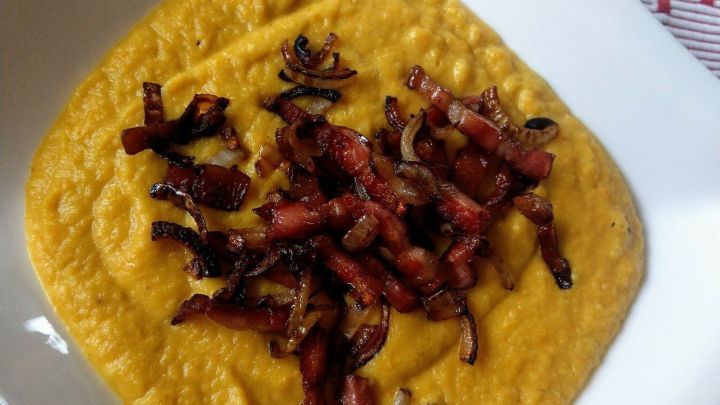 Steckr&uuml;benp&uuml;ree liegt cremig in einer Schale, garniert mit knusprigem Speck auf einem gemusterten Tischl&auml;ufer.