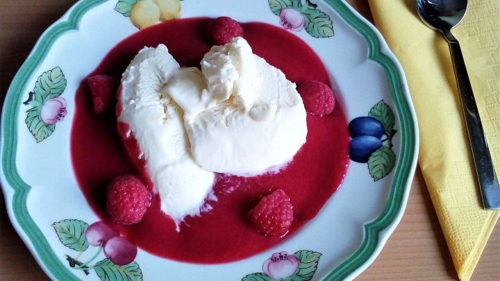 Ein wei&szlig;es Mousse liegt auf einem Himbeer-P&uuml;ree, umgeben von frischen Himbeeren, serviert auf einem dekorativen Teller.