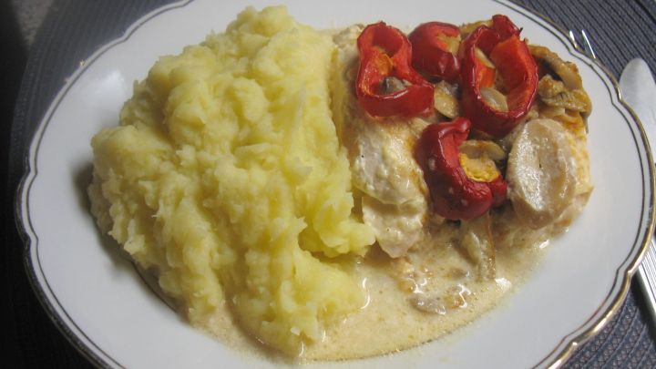 Zwiebel-Sahne-H&auml;hnchen-Auflauf mit zarten H&auml;hnchenst&uuml;cken, roten Paprika und cremiger Sauce neben einem Berg Kartoffelbrei.