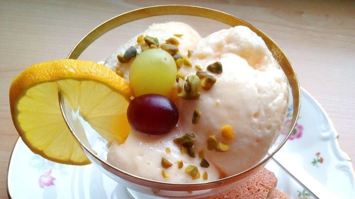 Eine Schale mit frischer Zitronencreme wird von frischen Fr&uuml;chten und Mandel-Eiwei&szlig;-Pl&auml;tzchen auf einem dekorativen Teller umgeben.