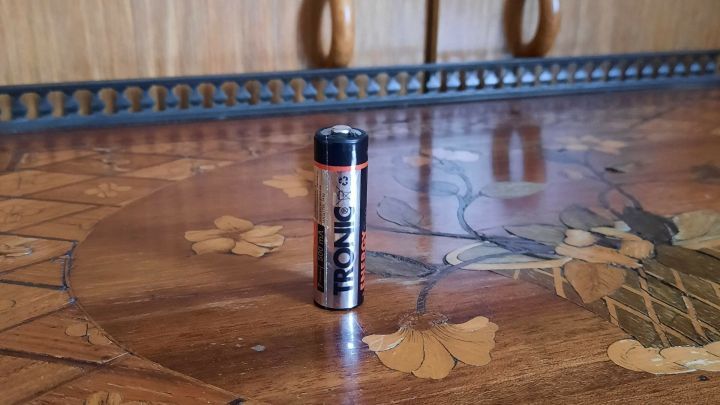 Eine Batterie steht auf einem kunstvoll verzierten Holztisch, umgeben von floralem Muster.