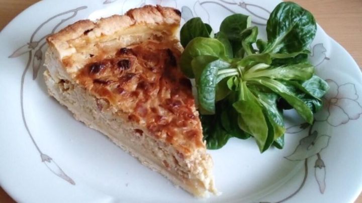 Ein St&uuml;ck Badischer Zwiebelkuchen liegt auf einem dekorativen Teller, umgeben von frischem Salat.