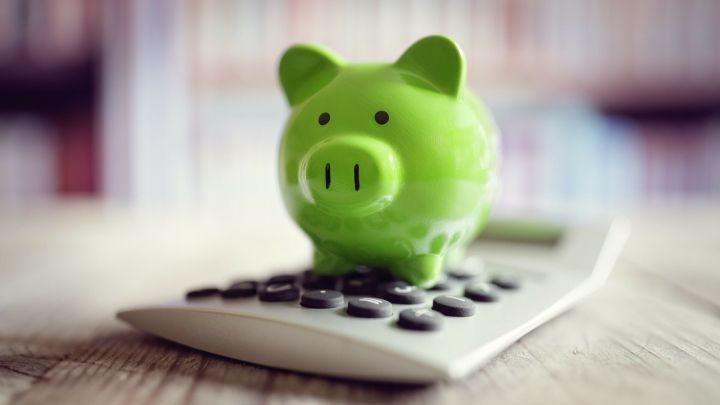 Ein gr&uuml;nes Sparschwein steht auf einem Taschenrechner, was zur Veranschaulichung von Geld sparen und Konsumverhalten dient.