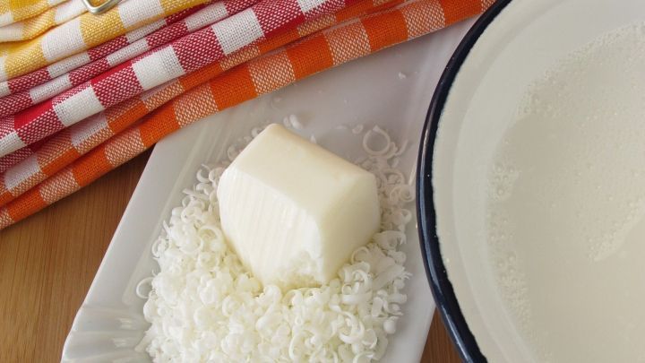Kernseife und geriebene seifenst&uuml;cke liegen auf einem Teller, umgeben von bunten K&uuml;chent&uuml;chern und einer Sch&uuml;ssel Wasser.