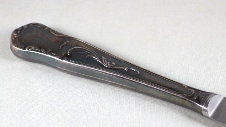 Ein silberner L&ouml;ffel liegt auf einer hellen Oberfl&auml;che und wird mit Zigarettenasche gereinigt, um seinen Glanz wiederherzustellen.