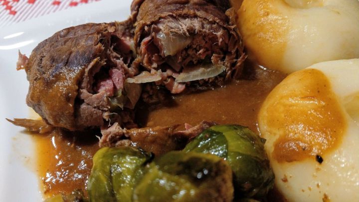 Zarte Rouladen liegen auf einem Teller, umgeben von Kartoffelkn&ouml;deln und Rosenkohl in kr&auml;ftiger So&szlig;e.