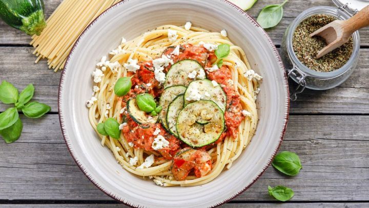 Spaghetti umgeben von Zucchini und Tomatenso&szlig;e, garniert mit Basilikum, in einer rustikalen Umgebung auf Holz.