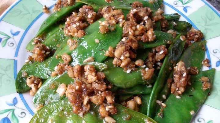 Zuckerschoten gl&auml;nzen in Butter, garniert mit knusprigen Sonnenblumenkernen und Sesam auf einem dekorativen Teller.