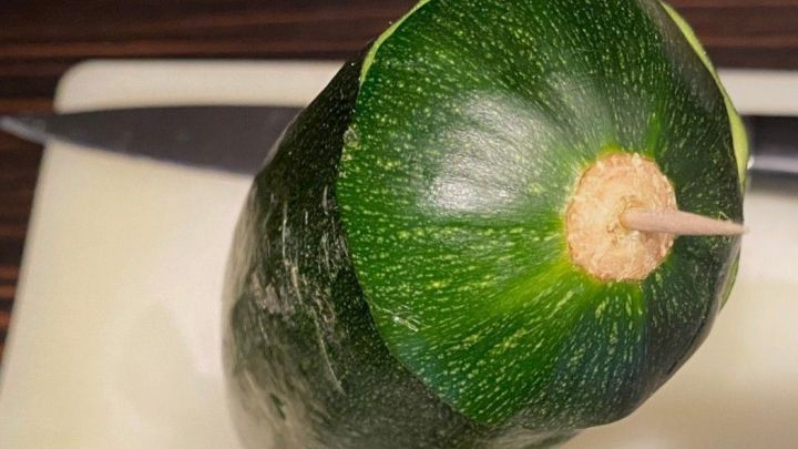 Eine Zucchini steht auf einem Schneidebrett, mit einem Zahnstocher gesichert, um Austrocknung zu verhindern.