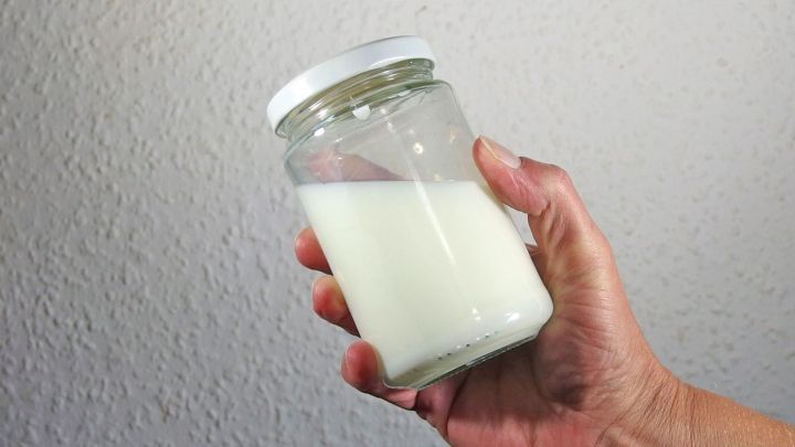 Ein Glas mit frischer Sahne wird von einer Hand gehalten, bereit zur Zubereitung von Butter selbst gemacht.